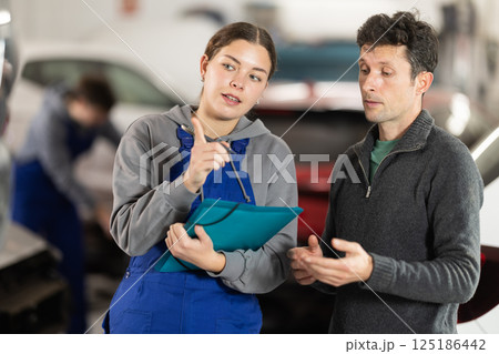 Girl employee asks clarifying questions and writes down male clients wishes regarding car repairs 125186442