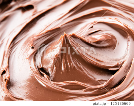 A rich and glossy close-up of chocolate frosting with smooth, creamy swirls. The texture and sheen highlight its deliciously thick and indulgent appearance, perfect for cakes and desserts. 125186669