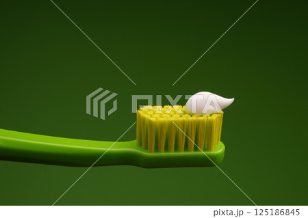 Green plastic toothbrush with white toothpaste on a green background. Oral health. Green plastic toothbrush with white toothpaste on a green background. Oral health. 125186845
