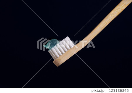 Bamboo toothbrush with transparent blue toothpaste on a dark blue background. Oral health. Bamboo toothbrush with transparent blue toothpaste on a dark blue background. Oral health. 125186846
