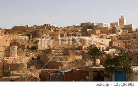 Earthen houses of Tamezret village with minaret of hilltop mosque 125186992