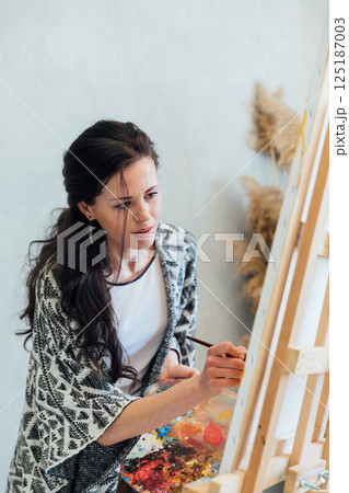 artist painting a picture on an easel with a brush with paints 125187003