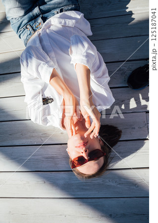 woman in sunglasses lying on wooden floor on beach 125187041