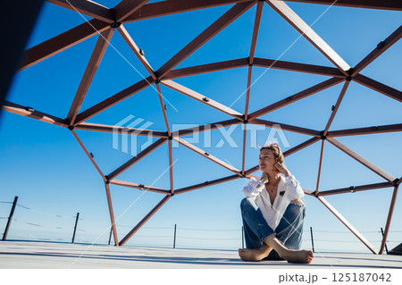 woman in sunglasses sitting on wooden floor on beach by sea 125187042