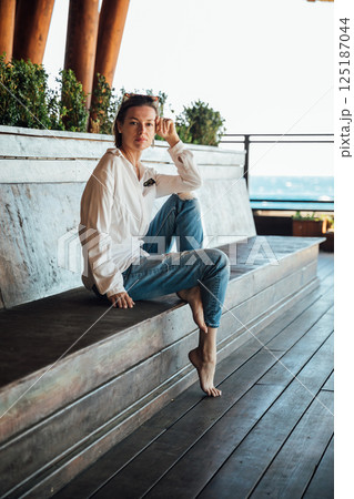 woman in sunglasses sitting on wooden floor on beach by sea 125187044