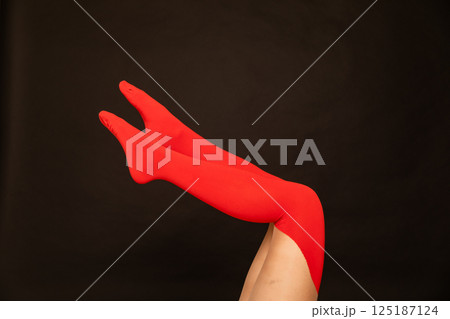 Slender long female legs in red stockings, tights on a black background 125187124