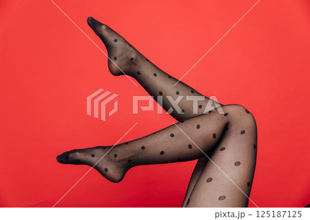 Slender female legs in black stockings, tights on a red background 125187125