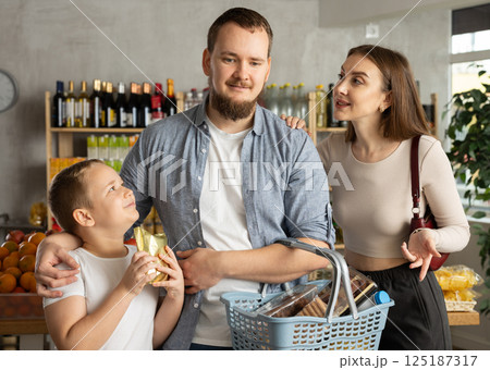 Family with various products in hands continuing shopping in grocery department of supermarket 125187317