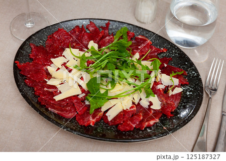 Thin slices of meat carpaccio, cheese and arugula on white plate. Traditional Italian dish 125187327