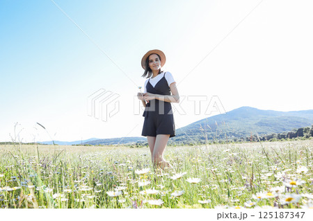 woman in dress walking with flowers in a field of daisies 125187347