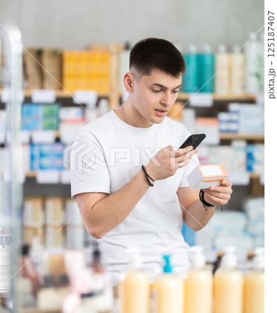 Handsome young guy choosing box with pills to improve well-being in pharmacy, scan QR code on label Handsome young guy choosing box with pills to improve well-being in pharmacy, scan QR code on label 125187407