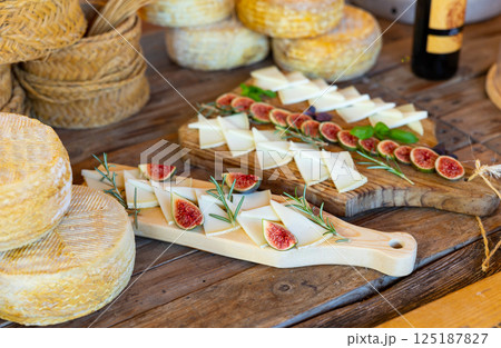 Slices of delicious cheese for degustation, served with figs and rosemary on a wooden table in winery 125187827