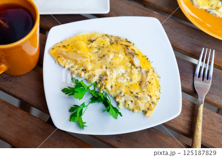 Fried omelette with chicken fillet pieces, cheese and greens 125187829