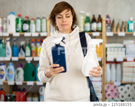 Positive female shopper carefully selects a spray glass cleaner for windows in home Positive female shopper carefully selects a spray glass cleaner for windows in home 125188155