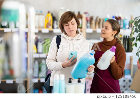 Female salesperson offers to buy a tile cleaner while a woman checks a QR code using smartphone Female salesperson offers to buy a tile cleaner while a woman checks a QR code using smartphone 125188450