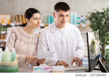 Male pharmacist helps girl buy medicine - he reads the prescription and compares it with data on computer Male pharmacist helps girl buy medicine - he reads the prescription and compares it with data on computer 125188460