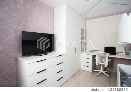 Modern workplace in the bedroom with white furniture, computer desk and chair. The TV is on a white chest of drawers. Bedroom interior. Modern workplace in the bedroom with white furniture, computer desk and chair. The TV is on a white chest of drawers. Bedroom interior. 125188529