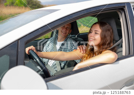 Cheerful girl driving car with boyfriend in passenger seat Cheerful girl driving car with boyfriend in passenger seat 125188763