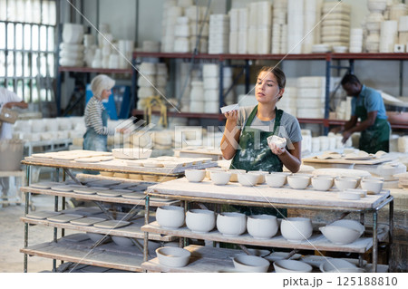Girl ceramist arranging new bowls in workshop 125188810