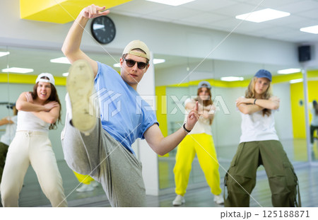 Ordinary teen girls and boy performing kick step movement during training together in dance school Ordinary teen girls and boy performing kick step movement during training together in dance school 125188871