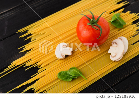 Fresh tomato, mushrooms, and spinach leaves on spaghetti, placed on a black table composition of pasta ingredients Fresh tomato, mushrooms, and spinach leaves on spaghetti, placed on a black table composition of pasta ingredients 125188916