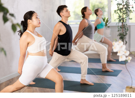 Young woman practicing warrior pose of yoga in light fitness room 125189011