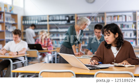 Schoolgirl studies on a laptop and writes notes in a copybook 125189224