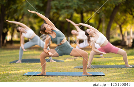 Slim women practicing yoga - virabhadrasana pose in summer park 125190843