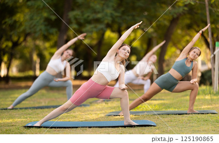 Slim women practicing yoga - virabhadrasana pose in summer park 125190865