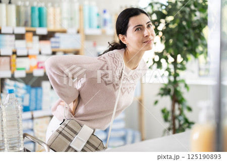 Girl suffers from back pain - looks for medicine in modern pharmacy 125190893