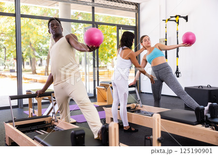 Positive woman and African-American man maintaining active lifestyle exercising with small pilates ball 125190901
