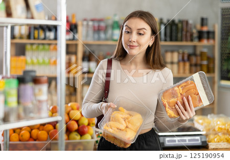 Female buyer carefully reads labels on packaging of semi-finished chicken products - she chooses best product in supermarket Female buyer carefully reads labels on packaging of semi-finished chicken products - she chooses best product in supermarket 125190954