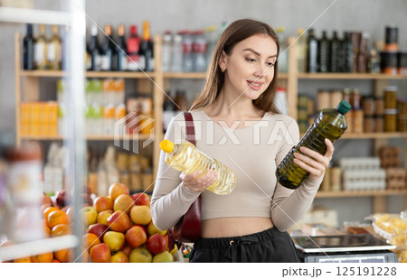 Girl buyer looks thoughtfully and indecisively at bottles of vegetable oil Girl buyer looks thoughtfully and indecisively at bottles of vegetable oil 125191228
