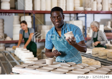 Positive man potter with new crafted crockry in workshop Positive man potter with new crafted crockry in workshop 125191249