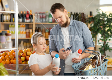 European man with son customer at shop scans QR code on milk bottle using phone camera European man with son customer at shop scans QR code on milk bottle using phone camera 125191280