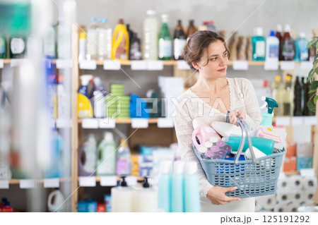 Woman with filled basket wanders around store, looking at display cases, seek something at counter 125191292