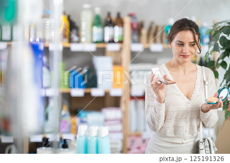 Young woman choosing eyeshadow and powder in store Young woman choosing eyeshadow and powder in store 125191326