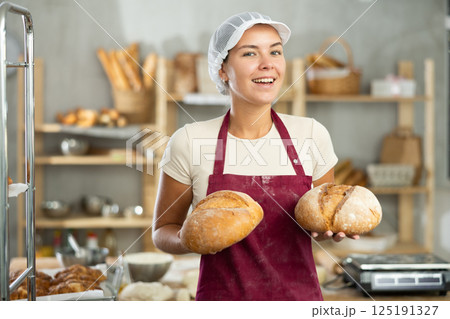 Smiling young female baker presenting fresh baked bread 125191327