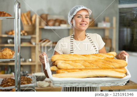 Smiling female baker presenting fresh baguettes in bakery Smiling female baker presenting fresh baguettes in bakery 125191346
