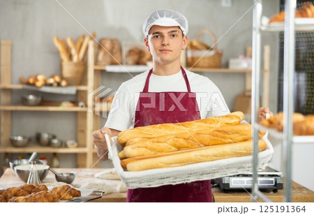 Young male baker holding baguettes in wicker basket Young male baker holding baguettes in wicker basket 125191364
