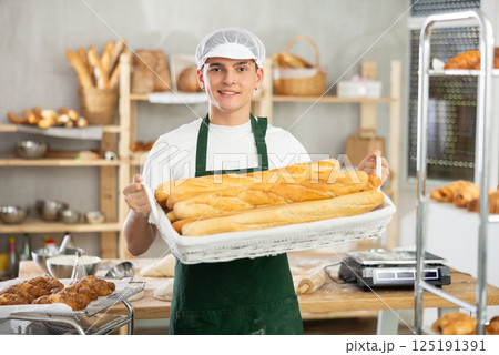 Happy male baker posing with basket of freshly baked baguettes in bakery, demonstrating concept of food industry and baker profession 125191391