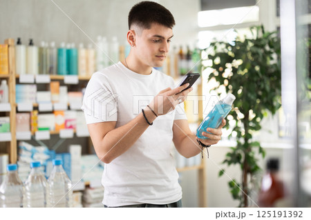 Positive young man buyer at pharmacy holding and choosing mouthwash, scan QR code on label 125191392