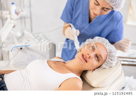 Young woman cosmetologist doing microcurrent procedure to young woman 125191495
