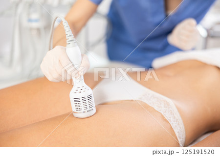 Young female cosmetologist performs whitening procedure on thighs of young woman 125191520