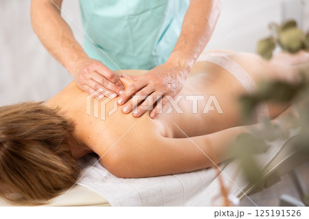 Woman dressed in tango panties receives massage of shoulder area, close-up, male masseur 125191526