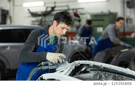 Male mechanic in uniform polishes bumper of car with machine in car service station Male mechanic in uniform polishes bumper of car with machine in car service station 125191608