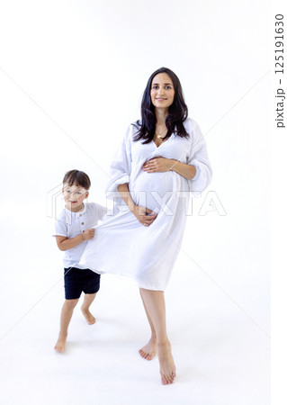 A young pregnant woman in a white dress with her cute son. A little boy gently hugs the belly 125191630