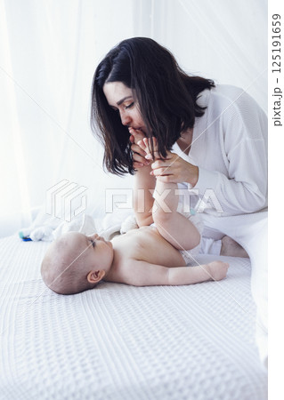 Pretty infant in a white bodysuit with his mom on a light background. Pretty infant in a white bodysuit with his mom on a light background. 125191659