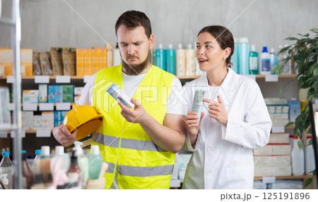 Laboring man builder buys gel for burns at pharmacy, consulting with girl pharmacist Laboring man builder buys gel for burns at pharmacy, consulting with girl pharmacist 125191896