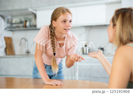 Smiling teenage girl talking friendly with woman in home kitchen 125191908